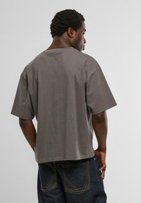 Pelēks īsajiem piedurknēm t-krekls ar brīvu piegriezumu, izgatavots no mīkstas kokvilnas. Iekļauj apkakli un gludu virsmu. Valkāts ar tumši zilām džinsām.