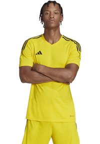 Geel sportshirt met korte mouwen, V-halsontwerp en zwarte drie-strepen accenten langs de schouders. Gemaakt van een gladde, ademende stof.