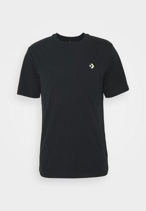 T-shirt noir à manches courtes et col rond avec un petit logo étoile jaune et chevron sur le côté gauche de la poitrine, présenté sur un fond blanc uni.