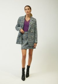Tweed blazer i blå, grøn og hvid med guldknapper, parret med en lilla top med blonder og en matchende minisød. Sorte ankelstøvler.