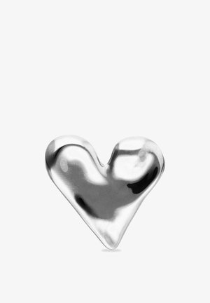 Objet en forme de cœur argenté, lisse et brillant, aux bords arrondis sur un fond blanc, reflétant la lumière et les ombres.