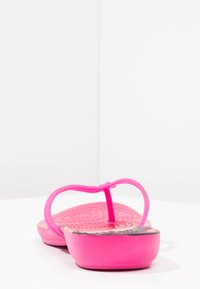 Ljusrosa flip-flop sandaler med hjärt-mönstrad sula på en vit yta mot en enkel vit bakgrund.