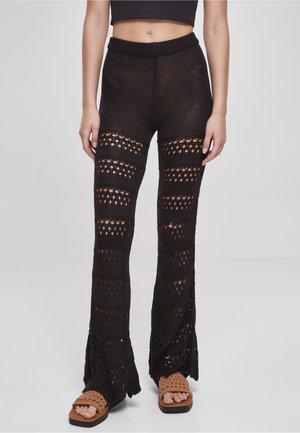 Femme portant un pantalon évasé en crochet noir avec des rayures ajourées horizontales, un crop top noir et des sandales tressées marron.