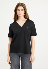 T-shirt nero a maniche corte con scollatura a V, realizzato in tessuto morbido, con un piccolo logo ricamato verde sul petto.