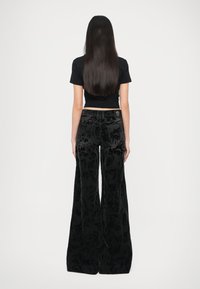 Črne žametne hlače z razširjenimi nogavicami in vzorčastim teksturiranim vzorcem, z nizkim pasom in dvema zadnjima žepoma. Nosi se s tesno prilegajočo se črno majico.