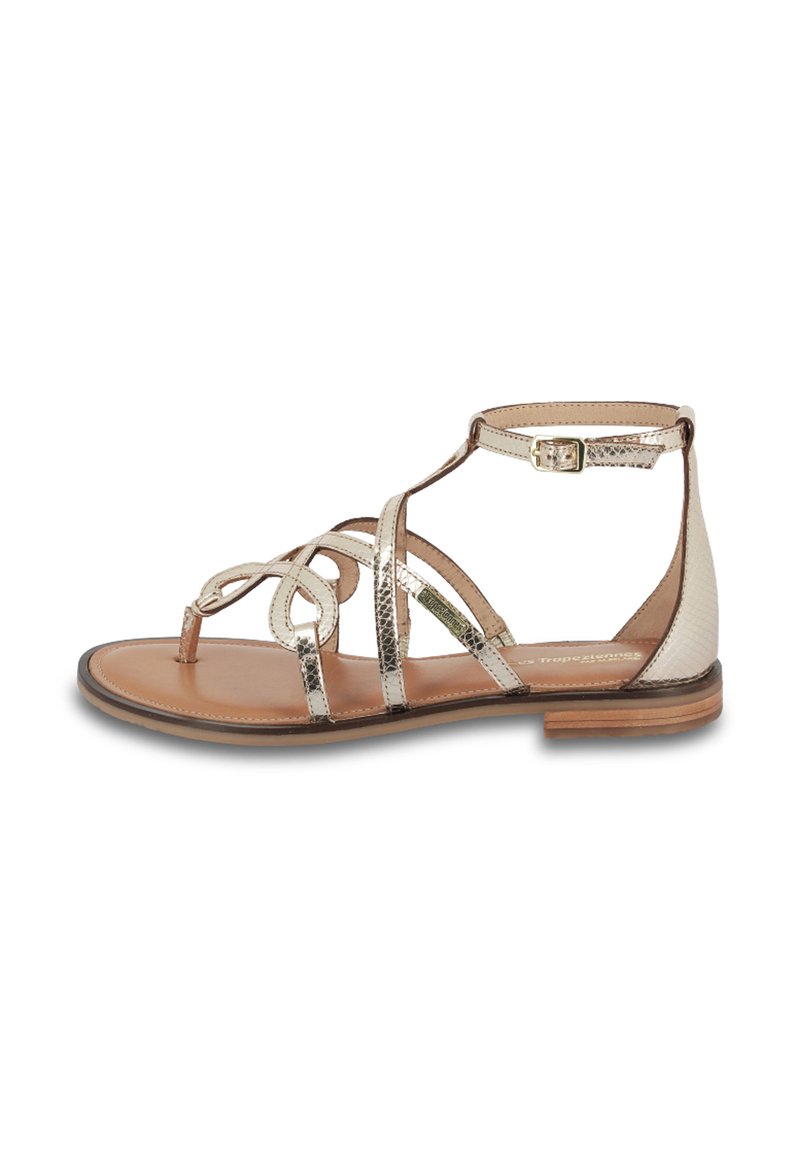 Sandalias planas con tiras ajustadas que cuentan con tiras metálicas plateadas y una base de cuero beige. Incluyen un cierre de hebilla y una textura suave.