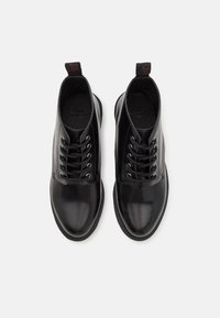 Bottes en cuir noir poli à lacets avec bouts ronds et languettes au talon, vues de dessus sur un fond blanc.
