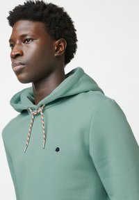 Lichtgroene hoodie van zacht materiaal, met een kangoeroezak, verstelbare drawstring met een gemusterd accent, en een klein boompje logo.
