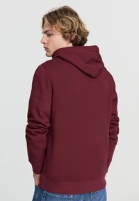 Felpa bordeaux realizzata in morbido misto cotone, con cappuccio regolabile e polsini a costine. Design semplice senza motivi o loghi visibili.