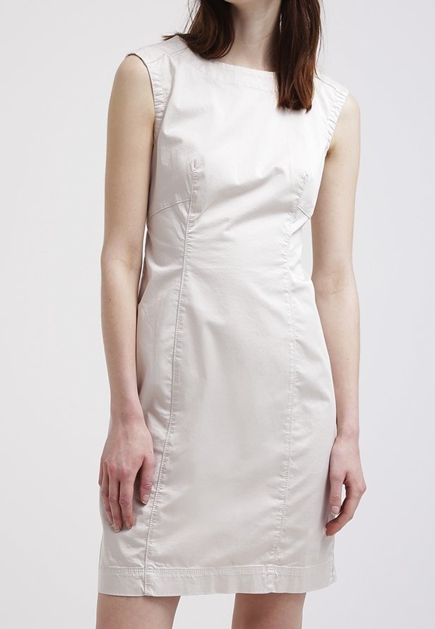 Över knäet, ärmlös klänning i ljus beige tyg. Har en rund halsringning, figursydd design och subtil sömdetaljering genom hela klänningen.