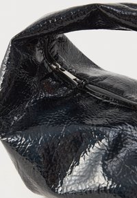Czarna torebka z lakierowanej skóry o pomarszczonej fakturze, z zamkiem błyskawicznym i okrągłym, miękkim uchwytem. Wymiary i proporcje są kompaktowe.