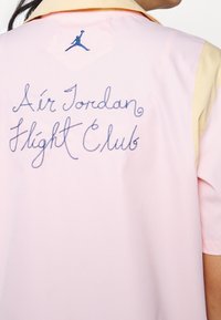 Personne portant une chemise rose et beige avec "Air Jordan Flight Club" brodé en bleu et un petit logo Jumpman sur le col arrière.