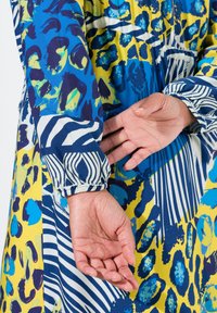 Multicolore jurk met een mix van dierenprints en strepen in blauw, geel en wit. Voorzien van elastische manchetten en vloeiende stof.