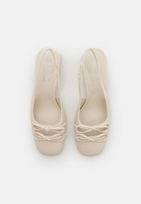 Pantofi slingback bej cu o textură netedă, vârf pătrat, fundițe decorative în față, și un toc scund, solid.