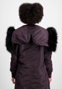 Ljubičasti vanjski odjevni predmet s elegantnim, podstavljenim dizajnom i crnim umjetnim krznom na ramenima. Ima rebraste manžete i zatvaranje na zip.