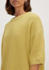 Übergroßer gelber Strickpullover mit Rundhalsausschnitt und kurzen Ärmeln. Weiche Textur mit gerippten Kanten und lockerer Passform.