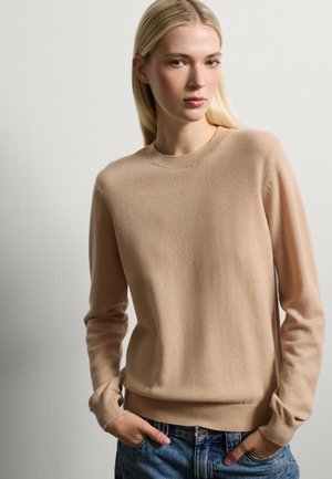 Beige wollen trui met een ronde hals, lange mouwen en ribgebreide manchetten en zoom. Casual gedragen met blauwe denim jeans.