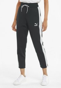 Pantalones deportivos negros con rayas laterales blancas, que cuentan con una cintura con cordón y un logo bordado. Fabricados con un tejido suave y texturizado. Longitud recortada.