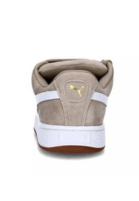 Sneaker beige in suede con dettagli bianchi, dotata di un colletto imbottito, logo dorato e suola in gomma bianca e marrone testurizzata.