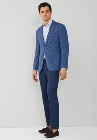 Blå textured blazer med en knapp, tillsammans med matchande skräddarsydda byxor. Ljusblå skjorta under och mörka loafer-skor.