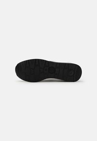 Suola delle scarpe con una superficie in gomma nera texturizzata, caratterizzata da un battistrada con motivo per la presa e due indentazioni circolari vicino al tallone.