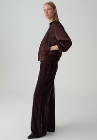 Brown bomber jacket with ribbed cuffs and hem, paired with wide-leg brown trousers. Smooth fabric with a relaxed fit. Black shoes complement the outfit.