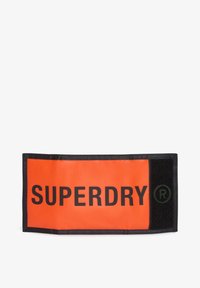 Jasnopomarańczowa tkanina z naszywką z czarnym napisem "SUPERDRY" i zielonym symbolem zarejestrowanego znaku towarowego, obszyta czarną nicią i z zapięciem na rzep.