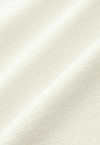 Tessuto bianco strutturato con un leggero motivo intrecciato, che presenta una superficie liscia e leggermente lucida, con pieghe cade.