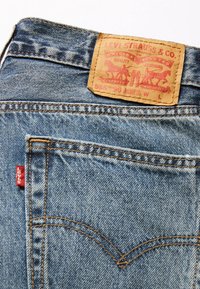 Blaue Levi's Jeans aus Denim, die die Gesäßtasche, das rote Levi's-Label und das beigefarbene Lederpatch mit Logo und Größenangaben zeigen.