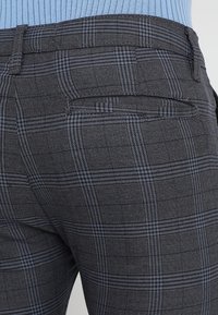 Šedé kostkované kalhoty s texturovanou tkaninou, slim fit, s jemným modrým vzorem a kapsou na zadní straně.