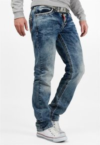 Jeans in denim blu con finitura sbiadita, taglio dritto, cuciture dettagliate e una cintura. Abbinati a sneaker bianche.