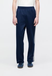 Navy plave sportske hlače s elastičnim pojasom, bijelim prugama sa strane i opuštenim krojem. Uparene s plavim tenisicama.