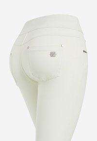 Jeans bianchi aderenti con vita alta, dotati di tasche posteriori e dettagli in metallo. Texture liscia con sottili dettagli di cucitura.