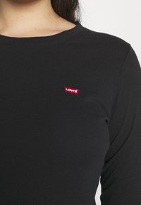 Schwarzes Langarmshirt aus weichem Stoff mit rundem Ausschnitt und einem kleinen roten Levi's Logo-Patch auf der linken Brust.