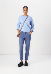 Sweatshirt azul claro com punhos elásticos, combinado com calças slim-fit azuis e mocassins pretos chunky. Uma mala cruzada castanha acentua o conjunto.