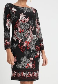 Svart knälång klänning med röda, vita och beige blommönster och paisleymönster, trekvartsärmar och rund halsringning.