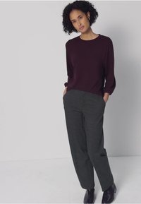 Vinröd långärmad topp kombinerad med grå, ledigt sittande byxor. Outfiten har en enkel design och slät textur, kompletterad med svart skor.