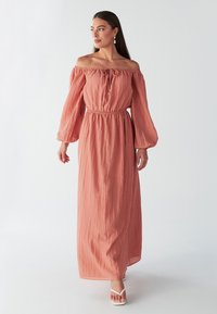 Robe maxi à épaules dénudées et manches longues en corail. Fabriquée en tissu froissé avec une taille élastique et un détail à nouer. Couleur slim avec des manches fluides.