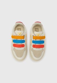 Beżowe trampki z czerwonymi akcentami, perforowanymi beżowymi nałożkami oraz trzema regulowanymi paskami na rzepy w kolorach pomarańczowym, niebieskim i żółtym. Gumowa podeszwa zewnętrzna.