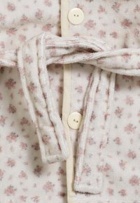 Ljusfärgad, texturerad tyg med rosa blommönster, som har ett knytmidja och en knappstängning. Mjuka och mysiga designelement.
