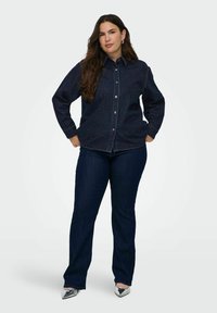 Dark denim button-up shirt with subtle speckled detail, paired with dark blue jeans and metallic pointed heels. Smooth texture and classic fit.