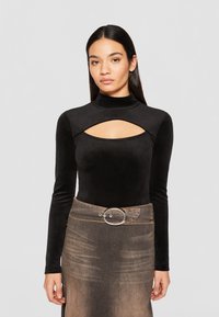 Black velvet long-sleeve top with a high neckline and cut-out detail. Paired with a brown denim skirt featuring a silver circular buckle.