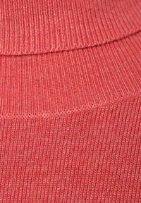 Korallinvärinen ribbineulottu kangas, jossa on korkeakauluksinen malli ja vuorottelevat vaakasuorat ja pystysuorat ribbikuviot.