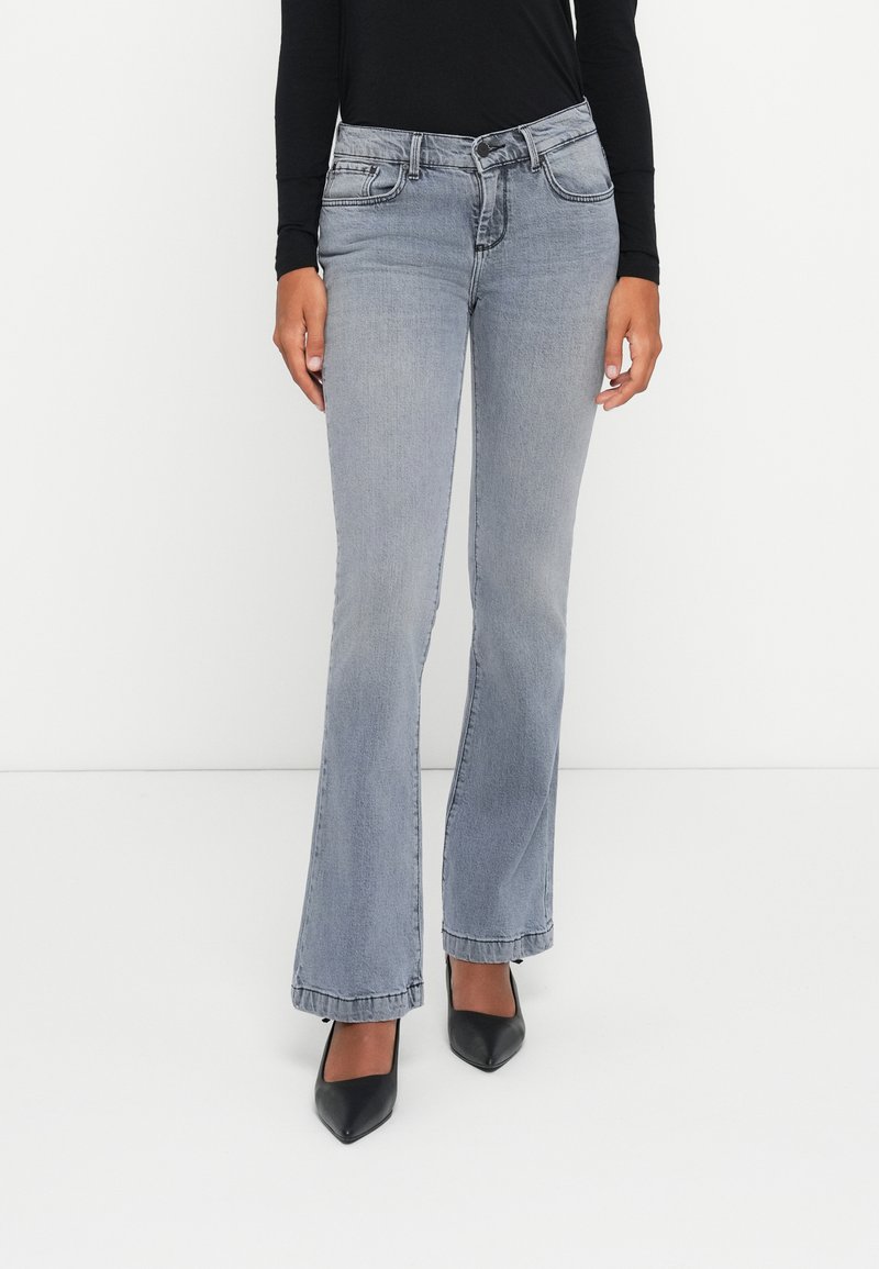 Jeans gris acampanados de mezclilla, con cinco bolsillos, cierre de botón y un desvanecimiento sutil. Combinados con tacones negros de punta afilada.