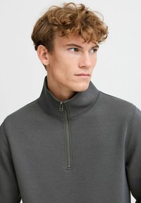 Gray zip-up sweatshirt made of smooth fabric. Features a high collar and quarter zipper. Seam detailing along shoulders.