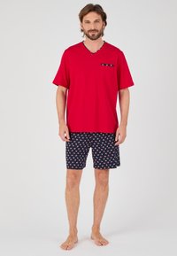 Rode katoenen V-hals T-shirt met een zak, gecombineerd met marineblauwe shorts met een witte ankerpatroon. Zachte stof, casual pasvorm.
