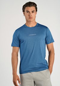 Blå t-shirt med korta ärmar i texturerat tyg, med rund halsringning och ordet "LINDBERGH" tryckt i vitt på framsidan.