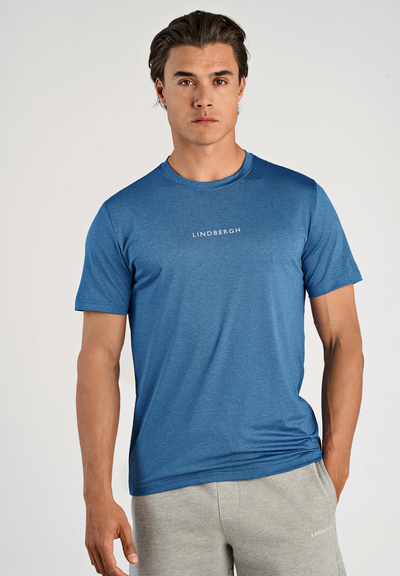 Blå t-shirt med korta ärmar i texturerat tyg, med rund halsringning och ordet "LINDBERGH" tryckt i vitt på framsidan.