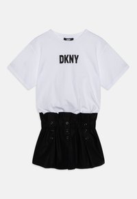 Šaty DKNY s bílým bavlněným topem ve stylu trička a černou skládací sukní. Sukně má stříbrné patentky a hladkou strukturu.