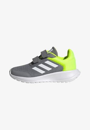 Chaussure de sport grise avec des accents vert néon lumineux, tige en mesh, rayures blanches et bandes Velcro. Semelle blanche flexible avec un relief texturé.